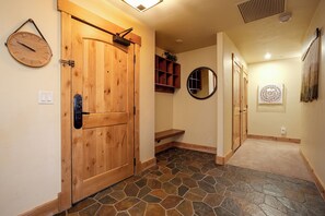 A hallway with a wooden door, a stone-tiled floor, a wall-mounted clock, a mirror, and a framed artwork. - BL6103 | Perfect for the Entire Family | 10 Hot Tubs | 4 Pools | Air Chilling (Steamboat Springs)