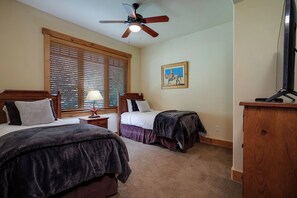 A bedroom with two beds, a ceiling fan, a painting, and a television on a wooden stand. - BL6105 | Spacious Mtn Condo | Private Hot Tub | Air Chilling | 4 Pools (Steamboat Springs)