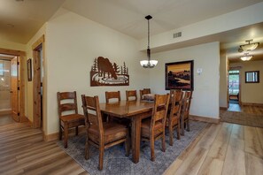 A dining room with a wooden table and chairs, a chandelier, and artwork on the walls. - BL6105 | Spacious Mtn Condo | Private Hot Tub | Air Chilling | 4 Pools (Steamboat Springs)