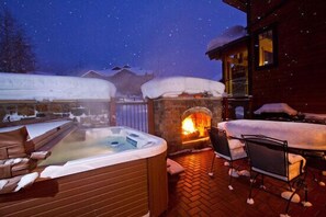 An outdoor hot tub area with a stone fireplace, surrounded by snow-covered buildings. - BL6105 | Spacious Mtn Condo | Private Hot Tub | Air Chilling | 4 Pools (Steamboat Springs)