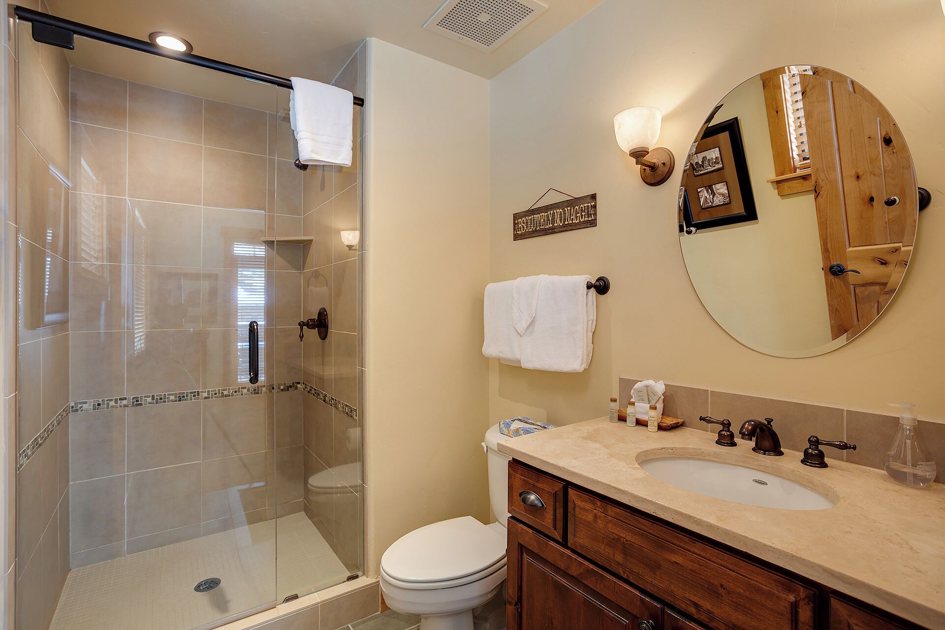 A bathroom with a glass shower enclosure, a toilet, a sink with a vanity, and a mirror.