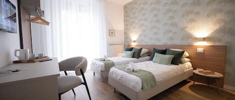 A hotel room with two beds, a desk, a chair, a small table, and a wall-mounted lamp.