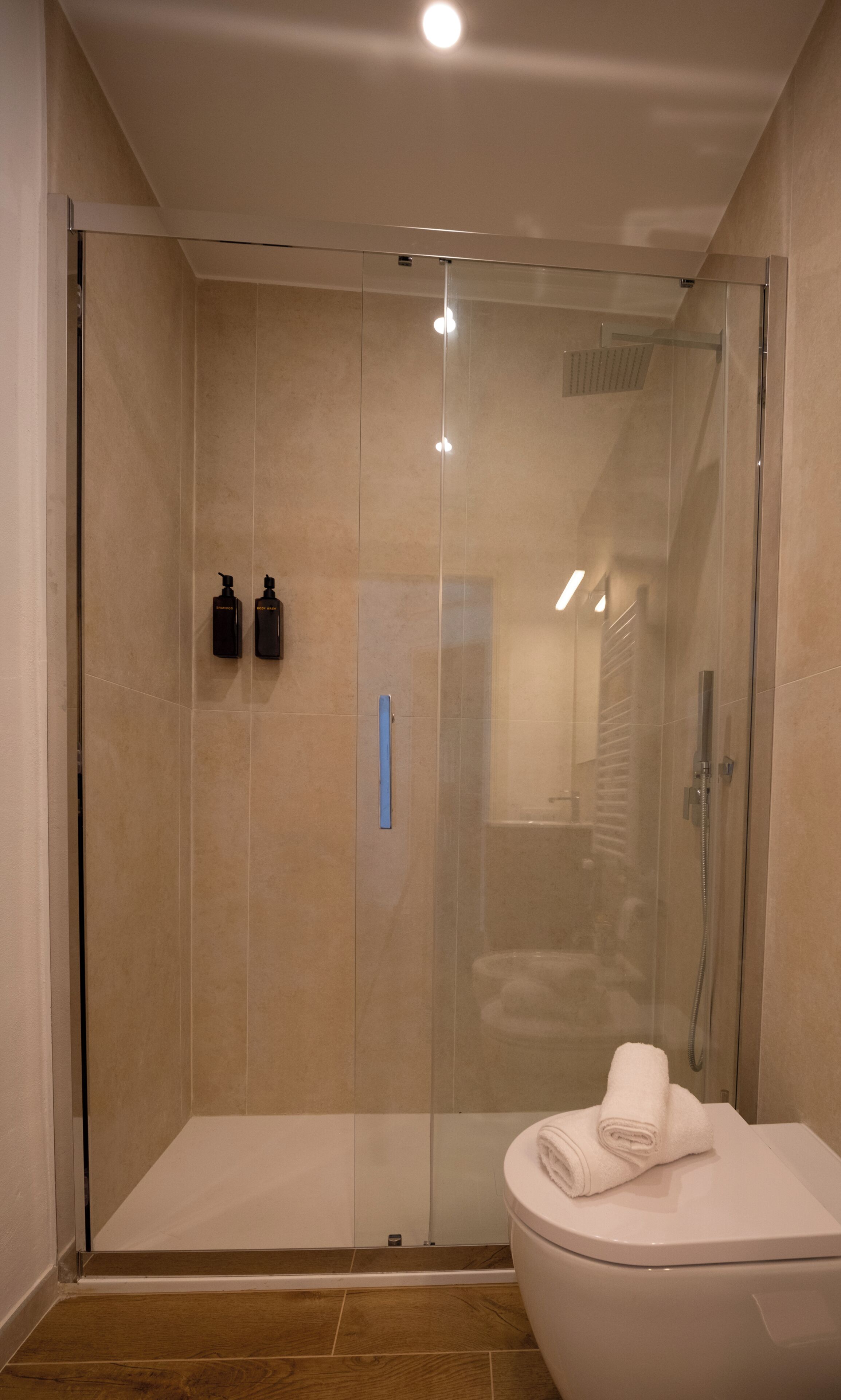 A modern bathroom with a glass-enclosed shower, a toilet, and two bottles of shampoo on the wall.