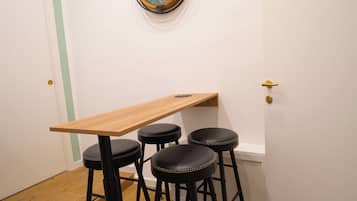 A small dining area with a wooden table and three black stools. A decorative wall clock hangs above the table.