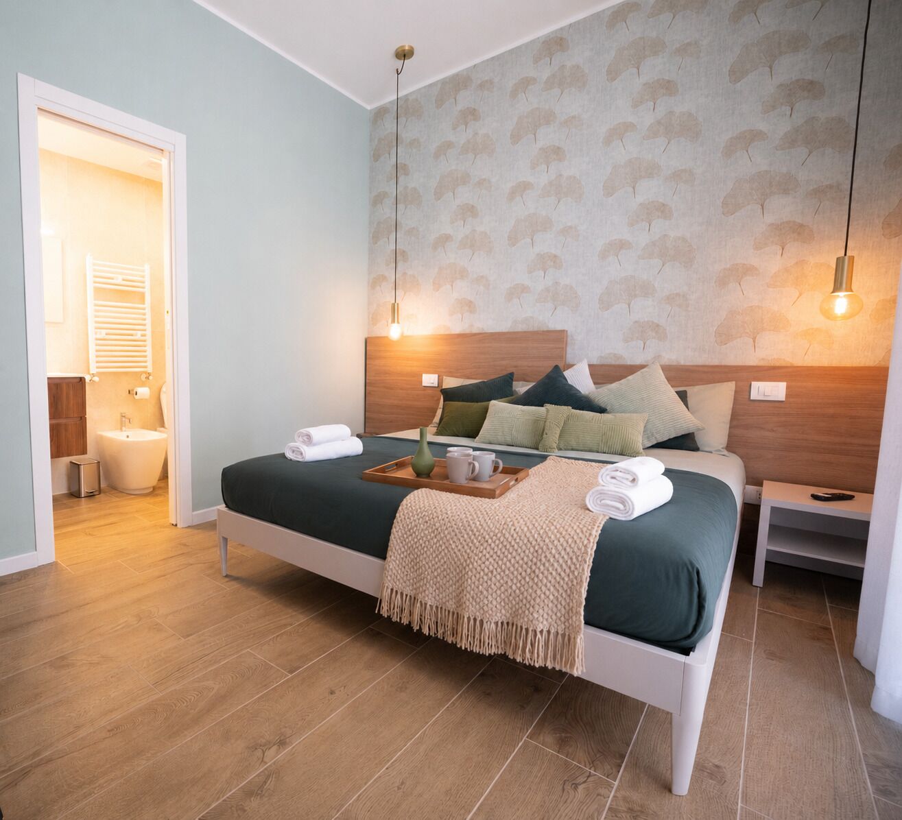 A hotel room with a bed, bedside tables, a nightstand, a wall-mounted light fixture, and a door leading to the bathroom.