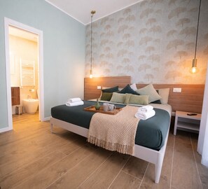 A hotel room with a bed, bedside tables, a nightstand, a wall-mounted light fixture, and a door leading to the bathroom. - Arcadia Rooms Palermo (Palermo)