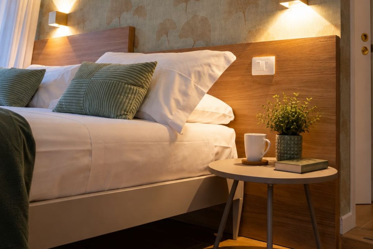 Una habitación de hotel con cama, mesita de noche y lámpara de pared.