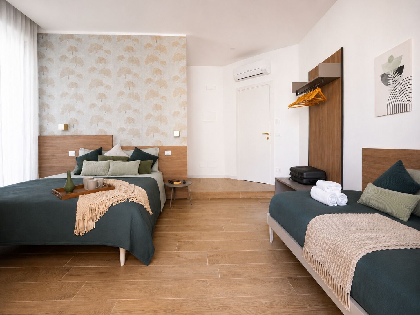 Habitación de hotel con dos camas, cabecera de madera, mesita de noche, armario y aire acondicionado de pared.