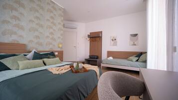 A hotel room with a bed, a desk, a chair, a wardrobe, and a small table with a tray.