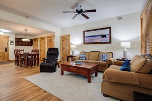 Ein Wohnzimmer mit Holzboden, Deckenventilator, Essbereich mit Holzstühlen und einem Tisch sowie ein großes gerahmtes Bild an der Wand.