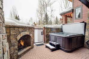 A stone fireplace with a fire, a hot tub, and a brick patio. - BL6108 | Ultimate Vacation Experience | Private Hot Tub | Air Chilling | Pools (Steamboat Springs)