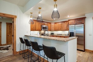 Eine moderne Küche mit Holzschränken, Edelstahlgeräten und einer zentralen Kochinsel mit Barhocker.