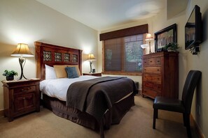 A bedroom with a large bed, two bedside tables with lamps, a wooden dresser, a chair, and a television on the wall. - BL6110 | Beautifully Appointed Mtn Condo | Private Hot Tub | Air Chilling | Pool (Steamboat Springs)
