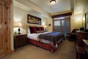 A bedroom with a large bed, two bedside tables, a desk, a chair, a window with blinds, and a painting on the wall. - BL6110 | Beautifully Appointed Mtn Condo | Private Hot Tub | Air Chilling | Pool (Steamboat Springs)
