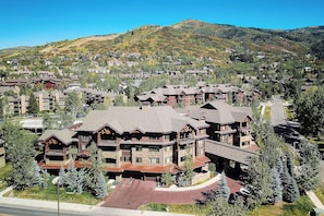 A large, multi-story lodge with a prominent front entrance, multiple balconies, and a mountainous backdrop. - BL6110 | Beautifully Appointed Mtn Condo | Private Hot Tub | Air Chilling | Pool (Steamboat Springs)