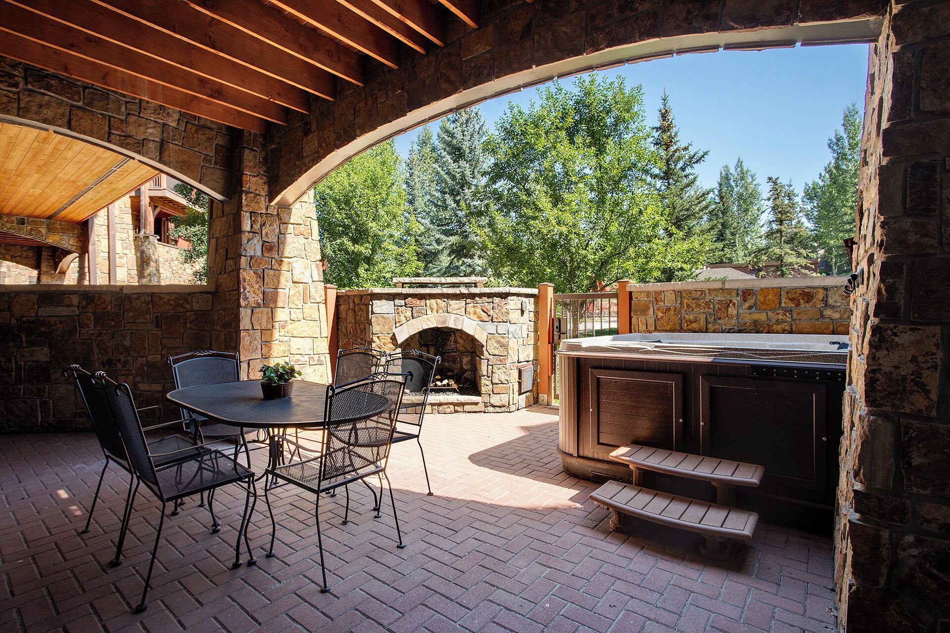 An outdoor patio with stone walls, a brick floor, and a stone fireplace.
