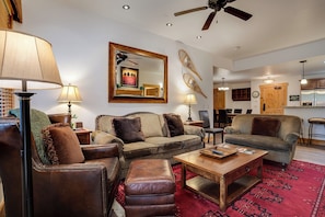 Ein geräumiges Wohnzimmer mit Ledersofas, einem Holztisch und einem roten Teppich mit Muster.