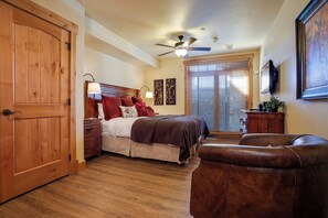 A bedroom with a wooden floor, a bed with red and white bedding, a ceiling fan, and a large window with blinds. - BL6111 | Private Courtyard with Hot Tub | Air Chilling | Pools | Wood Flooring (Steamboat Springs)