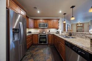 A modern kitchen with granite countertops, stainless steel appliances, and wooden cabinets. - BL6112 | Cozy Mtn Condo | Private Courtyard and Hot Tub | Air Chilling (Steamboat Springs)