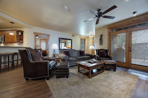 A spacious living room with a large ceiling fan, a dining area with wooden cabinets, and a large window with blinds. - BL6112 | Cozy Mtn Condo | Private Courtyard and Hot Tub | Air Chilling (Steamboat Springs)