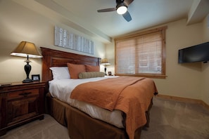 A bedroom with a bed, two bedside tables, a ceiling fan, a window with blinds, and a flat-screen TV mounted on the wall. - BL6112 | Cozy Mtn Condo | Private Courtyard and Hot Tub | Air Chilling (Steamboat Springs)