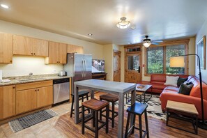 A compact kitchen with wooden cabinets, a stainless steel refrigerator, and a dining area with stools. - BL6113 | Gorgeous Condo | Easy Walk to Slopes | 10 Hot Tubs | Winter Shuttle (Steamboat Springs)