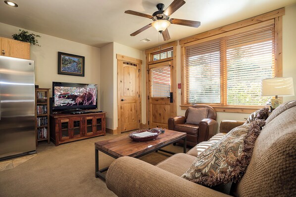 A living room with a television, wooden furniture, a ceiling fan, and large windows with blinds. - BL6115 | Unique and Beautiful Getaway | Heated Garage| Hot Tubs | Air Chilling (Steamboat Springs)