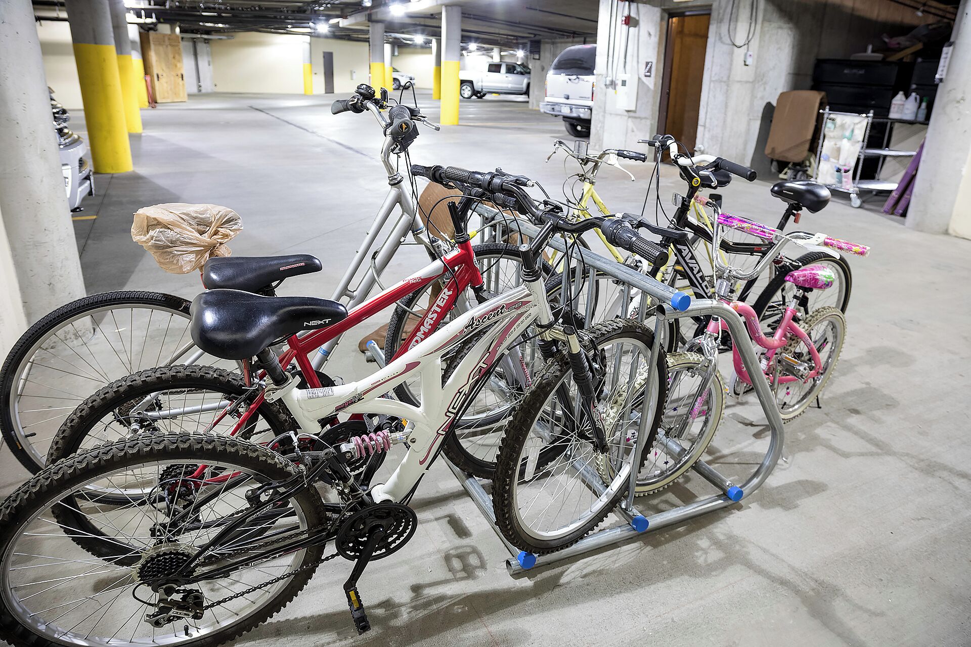 Bicycles parked in a multi-level parking garage with concrete floors and yellow pillars.