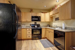 Eine Küche mit Holzschränken, einem schwarzen Kühlschrank, einer Mikrowelle, einem Backofen, einem Geschirrspüler und Granit Arbeitsplatten.