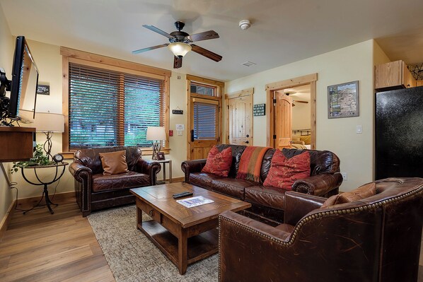 A cozy living room with a brown leather sofa, two armchairs, a wooden coffee table, and a ceiling fan. - BL6116 | Charming Garden Apartment | Walk to Mtn | Air Chilling | 4 Pools (Steamboat Springs)