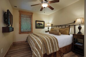 A bedroom with a bed, a ceiling fan, a window with blinds, a bedside table with a lamp, and a wall-mounted TV. - BL6116 | Charming Garden Apartment | Walk to Mtn | Air Chilling | 4 Pools (Steamboat Springs)