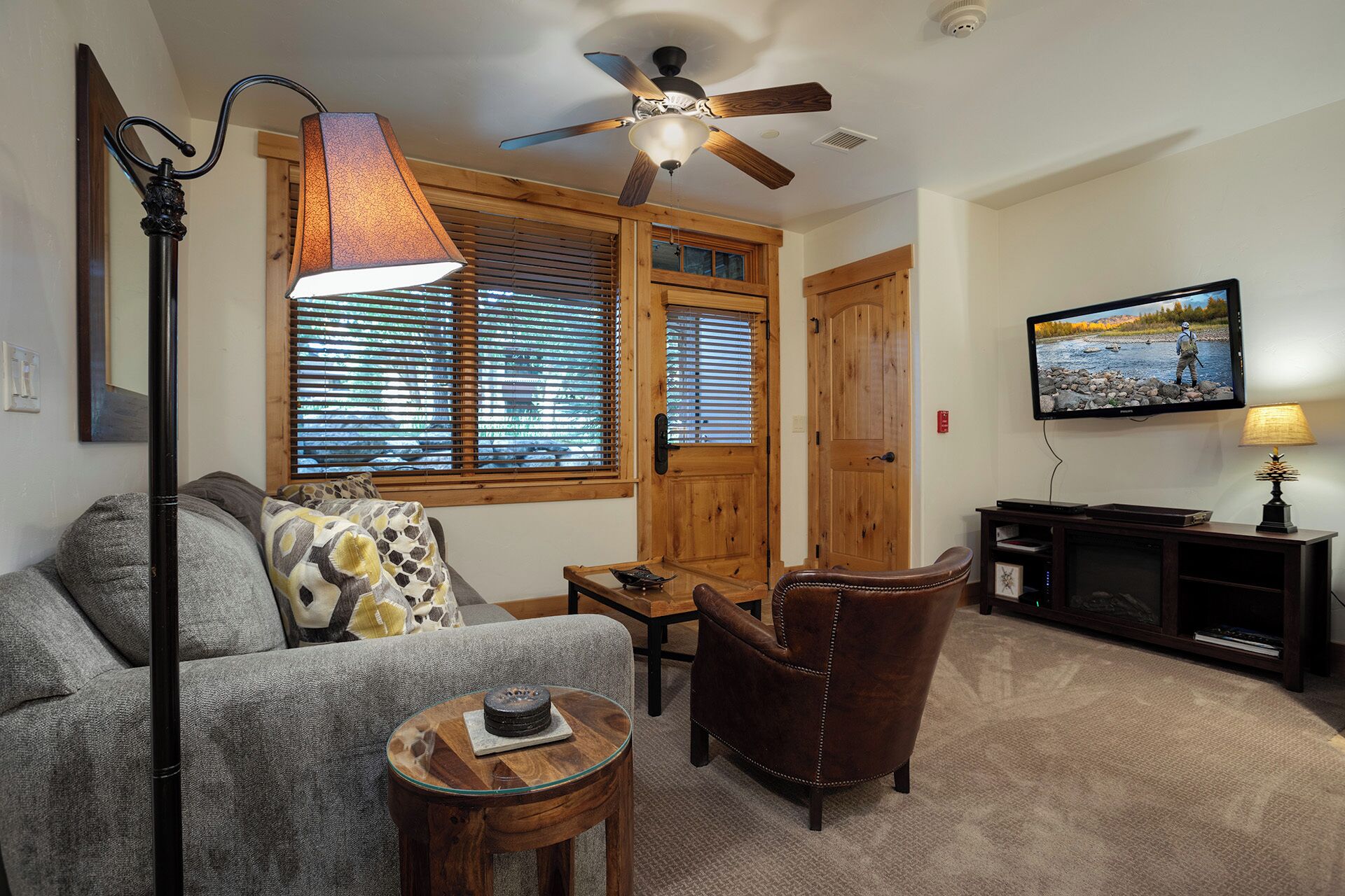 A living room with a sofa, armchair, coffee table, and a television mounted on the wall.