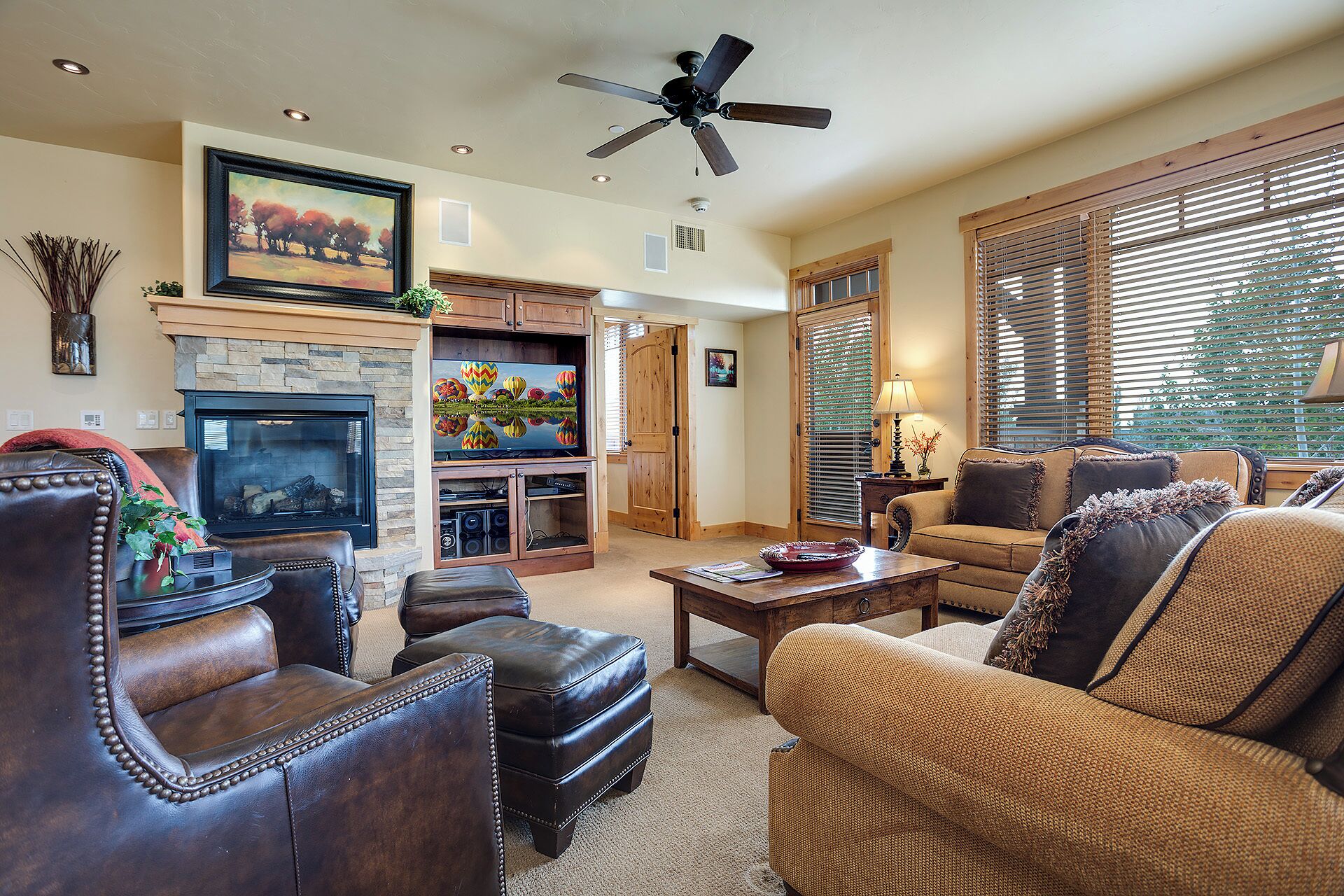 A living room with leather furniture, a fireplace, a television, and a ceiling fan.