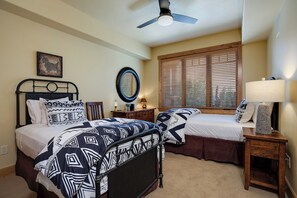 A bedroom with two beds, a ceiling fan, a large window with blinds, a mirror, and a lamp on a wooden nightstand. - BL6202 | Perfect for the Entire Family | Hot Tubs and Pools | Air Chilling (Steamboat Springs)