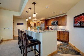 A kitchen with a central island, wooden cabinets, a microwave, and a refrigerator. - BL6202 | Perfect for the Entire Family | Hot Tubs and Pools | Air Chilling (Steamboat Springs)