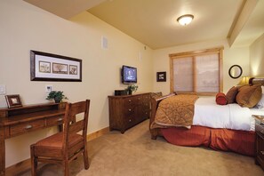 A bedroom with a bed, a desk, a chair, a dresser, a television, and a window with blinds. - BL6203 | Beautiful Sunset Views| 10 Hot Tubs | Air Chilling | 4 Pools (Steamboat Springs)
