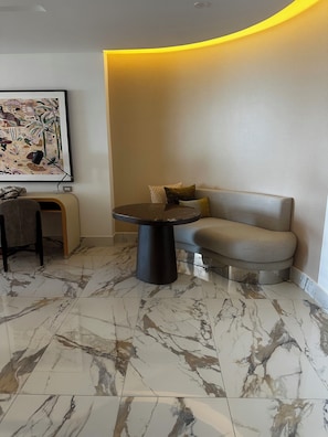 A modern living room with a marble floor, a round table, a sofa, and a framed artwork on the wall.