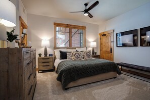 A bedroom with a bed, two bedside tables, a wooden dresser, a ceiling fan, a window with blinds, and a door. - BL6205 | Unparalleled Luxury at Bear Lodge | Close to Skiing | Air Chilling (Steamboat Springs)