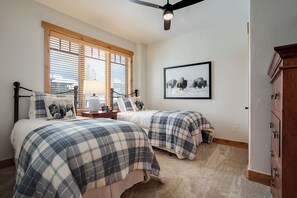 A bedroom with two beds, a ceiling fan, a window with blinds, a bedside table with a lamp, and a framed picture on the wall. - BL6205 | Unparalleled Luxury at Bear Lodge | Close to Skiing | Air Chilling (Steamboat Springs)