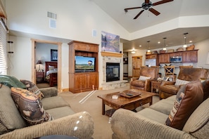 A spacious living room with a fireplace, leather sofas, a television, and a kitchen area with wooden cabinets. - BL6302 | Top Floor with Stellar Views | Short Walk to Mtn | Air Chilling (Steamboat Springs)