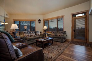 A living room with a brown leather sofa, two armchairs, a coffee table, and a rug. There are two windows with blinds, a door, and a wall clock. - BL6302 | Top Floor with Stellar Views | Short Walk to Mtn | Air Chilling (Steamboat Springs)