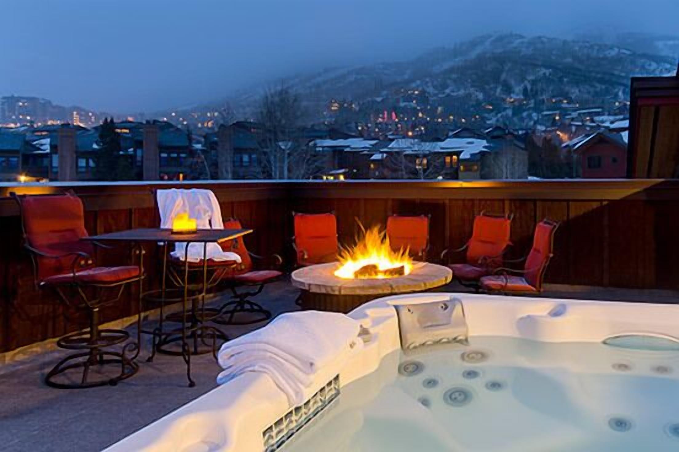 A hot tub with a fire feature, surrounded by red chairs and a table with a candle.
