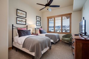 A bedroom with two beds, a ceiling fan, a television, and a window with blinds. - BL6303 | Semi Private Roof Top Patio | Unreal View | 4 Pools| Air Chilling (Steamboat Springs)