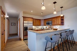 Cozinha moderna com armários de madeira, eletrodomésticos de aço inoxidável, bancada de granito e banquetas.