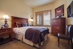 A bedroom with a large bed, wooden headboard, two bedside tables with lamps, a dresser, a chair, and a window with blinds. - BL6308 | Top floor Condo with Vaulted Ceilings | Pools | Views | Air Chilling (Steamboat Springs)