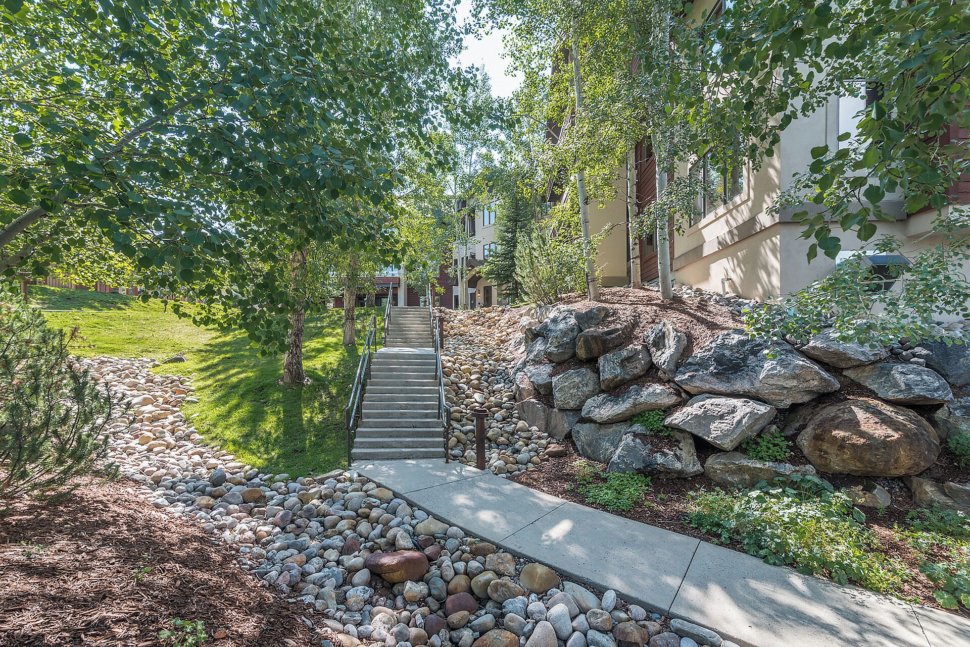 A pathway leading to a building with a stone wall and a metal railing.