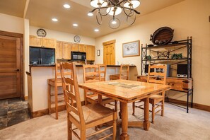 A dining area with a wooden table and chairs, a kitchen with wooden cabinets, a microwave, and a ceiling light fixture. - CL3101 | Comfortable Mountain Vibes | A/C | 10 Hot Tubs | 4 Pools (Steamboat Springs)