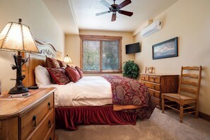 A bedroom with a bed, a wooden dresser, a desk, a chair, a ceiling fan, a TV, a window with blinds, and a painting on the wall. - CL3101 | Comfortable Mountain Vibes | A/C | 10 Hot Tubs | 4 Pools (Steamboat Springs)
