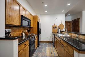 Una cocina con gabinetes de madera, un refrigerador negro, un microondas, una cafetera y un fregadero.