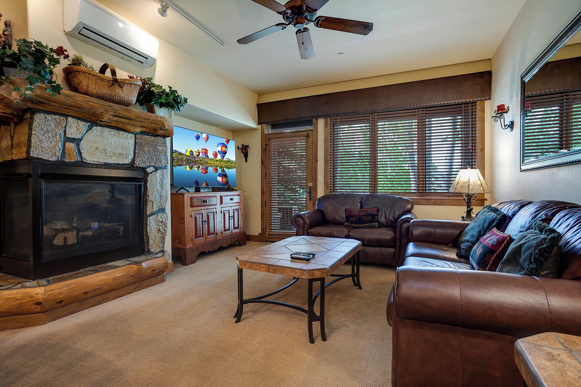 A cozy living room with a fireplace, leather furniture, and a television displaying hot air balloons.